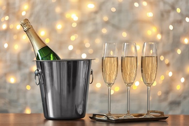 Glasses with champagne and bottle in bucket on table against blurred lights