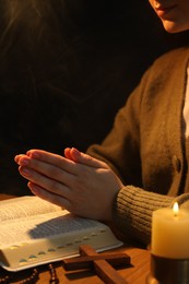 Photo of Woman praying at table with burning candle and Bible, closeup