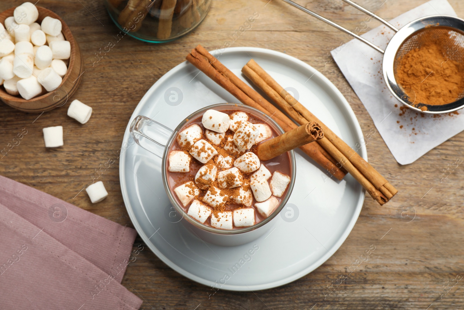 Photo of Glass cup of hot cocoa with aromatic cinnamon and marshmallows on wooden table, flat lay