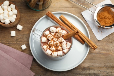 Photo of Glass cup of hot cocoa with aromatic cinnamon and marshmallows on wooden table, flat lay