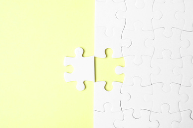 Photo of Blank white puzzle with separated piece on yellow background, flat lay