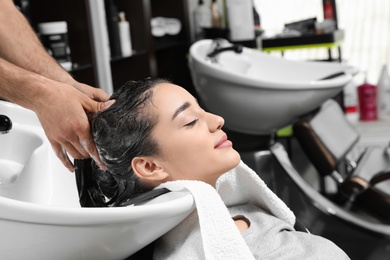 Stylist washing client's hair at sink in beauty salon