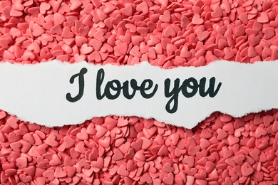 Photo of Handwritten message I Love You on pink heart shaped sprinkles, top view