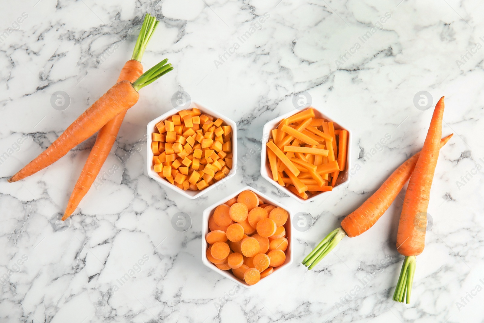 Photo of Bowls with cut carrot in different ways and fresh vegetable on marble table, top view