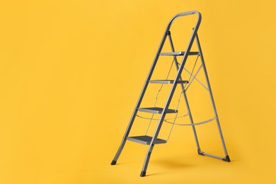 Photo of Modern metal stepladder on yellow background. Space for text