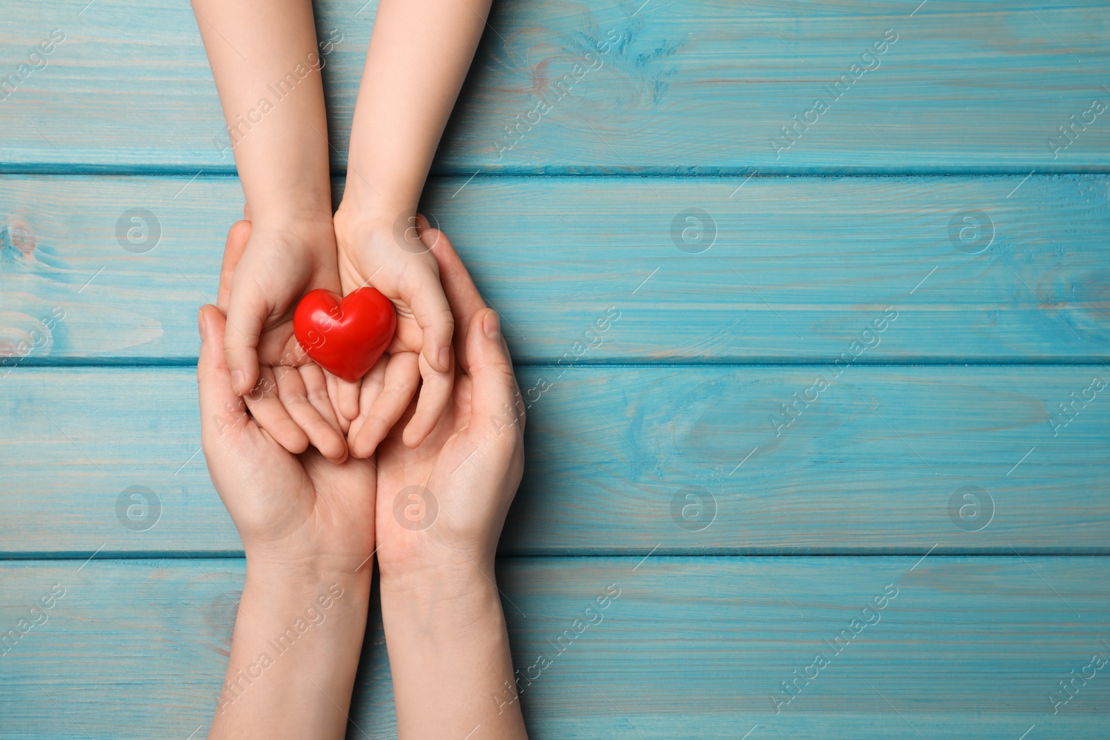 Photo of Woman and kid holding red heart in hands at light blue wooden table, top view. Space for text