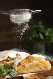 Photo of Sprinkling powdered sugar onto pieces of delicious apple strudel on wooden board, closeup