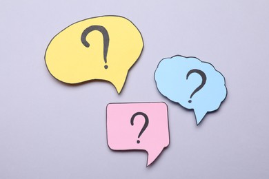 Photo of Different paper speech bubbles with question marks on light grey background, flat lay