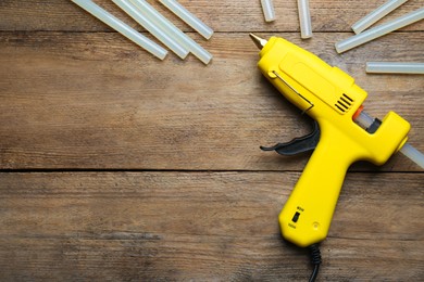 Photo of Yellow glue gun and sticks on wooden table, flat lay. Space for text