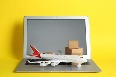 Photo of Laptop, airplane model and carton boxes on yellow background. Courier service