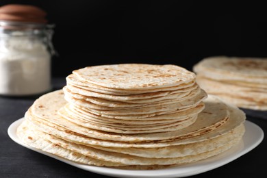 Many tasty homemade tortillas on black wooden table, closeup