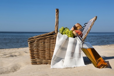 Photo of Basket with food and bottle of wine on beach. Summer picnic