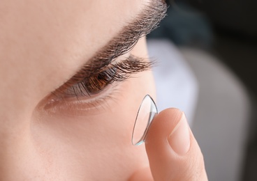 Photo of Young woman putting contact lens in her eye, closeup