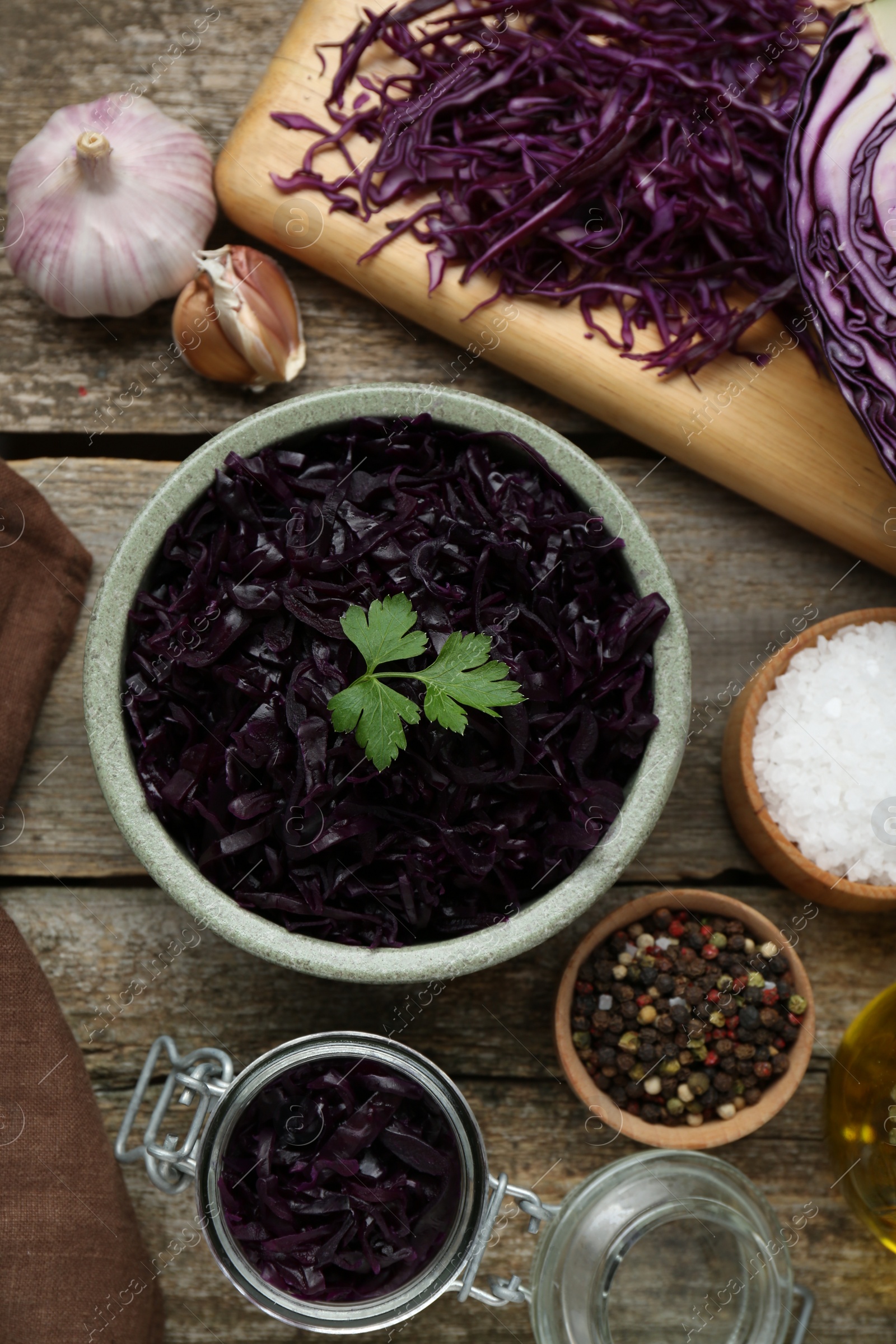 Photo of Tasty red cabbage sauerkraut with parsley and different ingredients on wooden table, flat lay