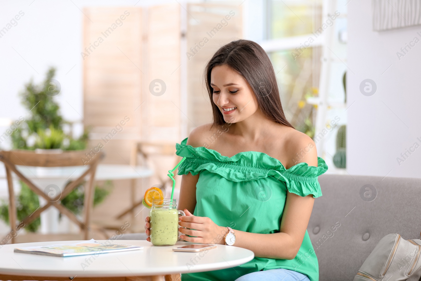 Photo of Young woman with tasty healthy smoothie at table, indoors