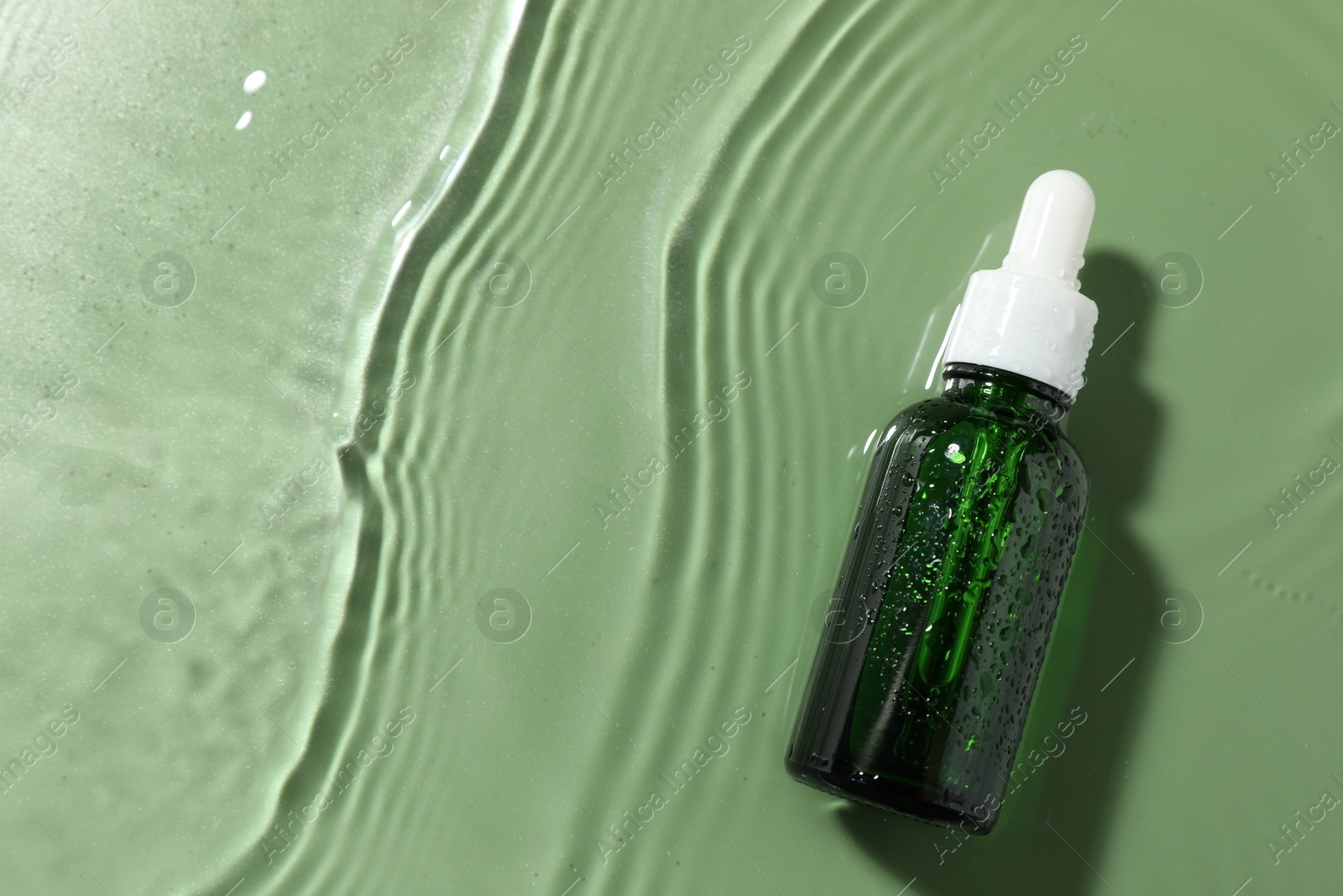 Photo of Bottle of cosmetic product in water on pale green background, top view. Space for text