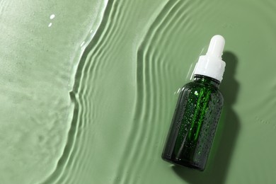 Bottle of cosmetic product in water on pale green background, top view. Space for text