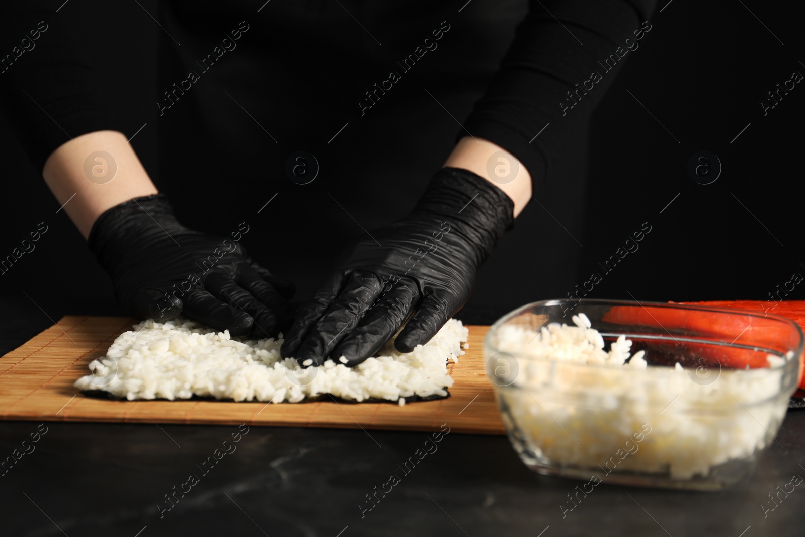 Photo of Chef in gloves making sushi roll at dark table, closeup