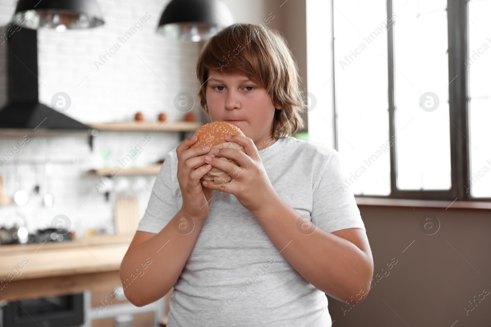 Photo of Overweight boy with tasty burger in kitchen