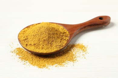 Photo of Curry powder in spoon on white wooden table