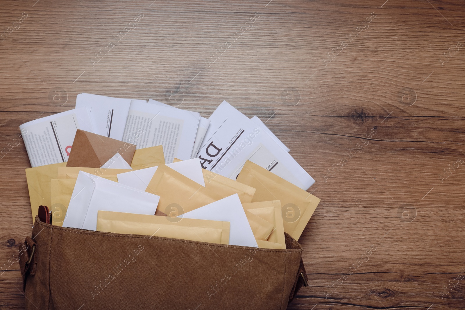 Photo of Brown postman bag with newspapers and mails on wooden table, flat lay. Space for text