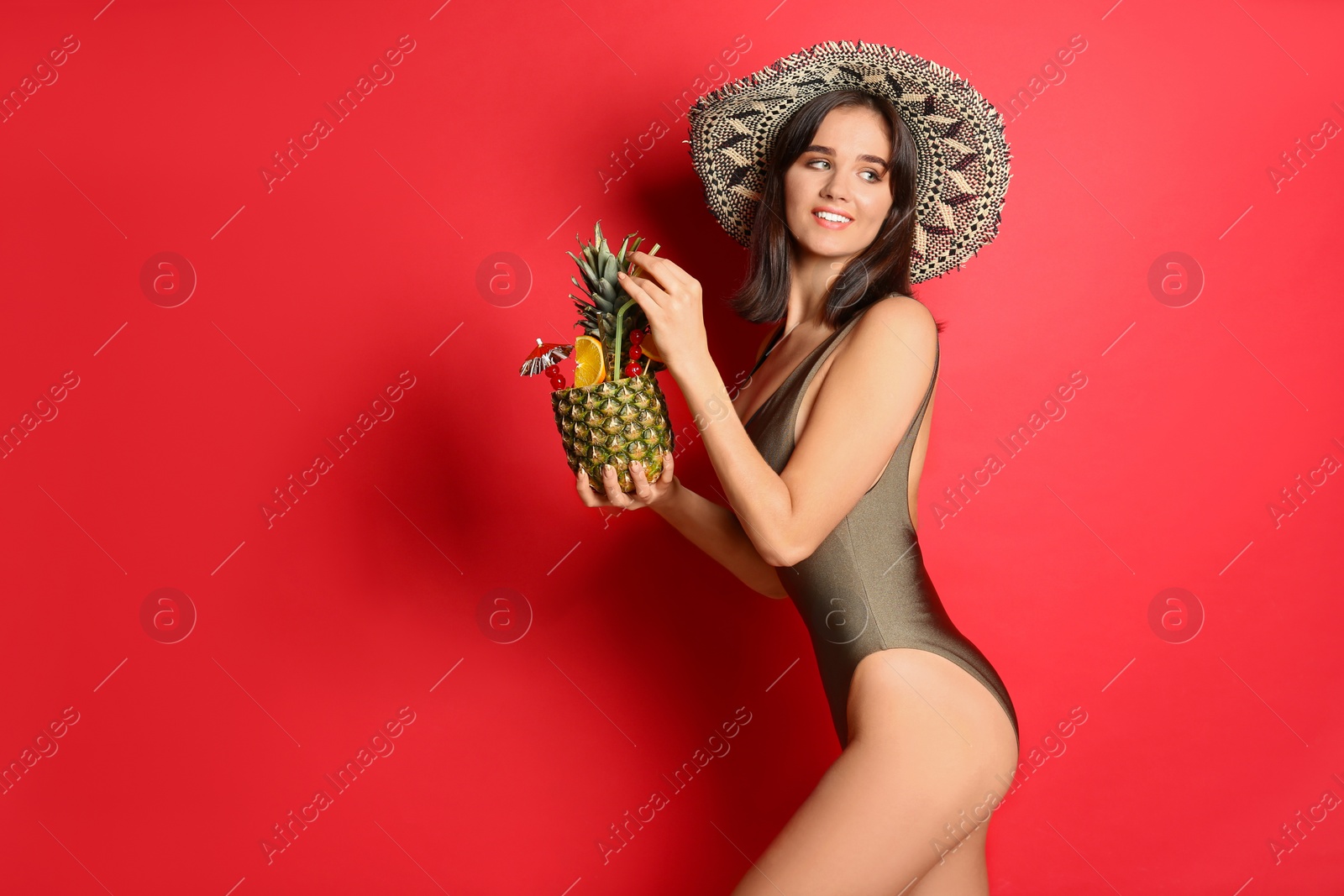 Photo of Beautiful woman in stylish swimsuit holding tropical cocktail on red background. Space for text