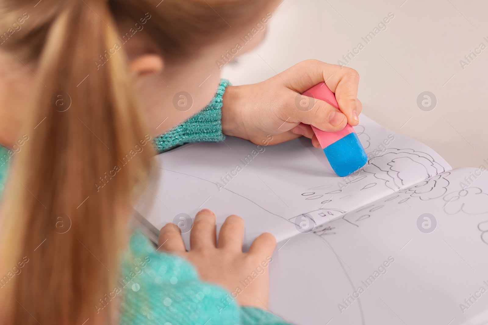 Photo of Girl erasing drawing in her book at white desk, closeup