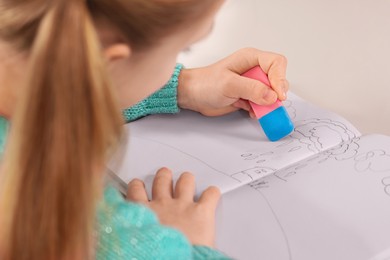 Girl erasing drawing in her book at white desk, closeup