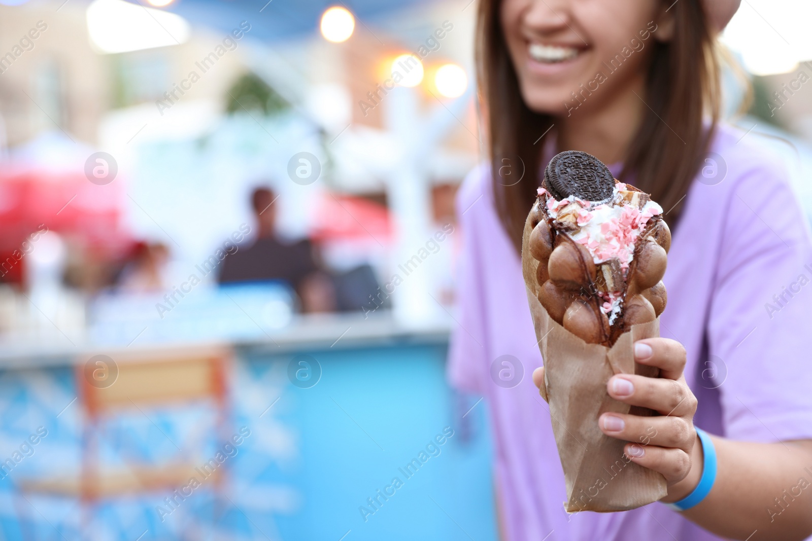 Photo of Young woman holding delicious sweet bubble waffle with ice cream outdoors, closeup