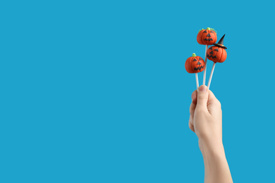 Woman with delicious pumpkin shaped cake pops and space for text on light blue background, closeup. Halloween celebration