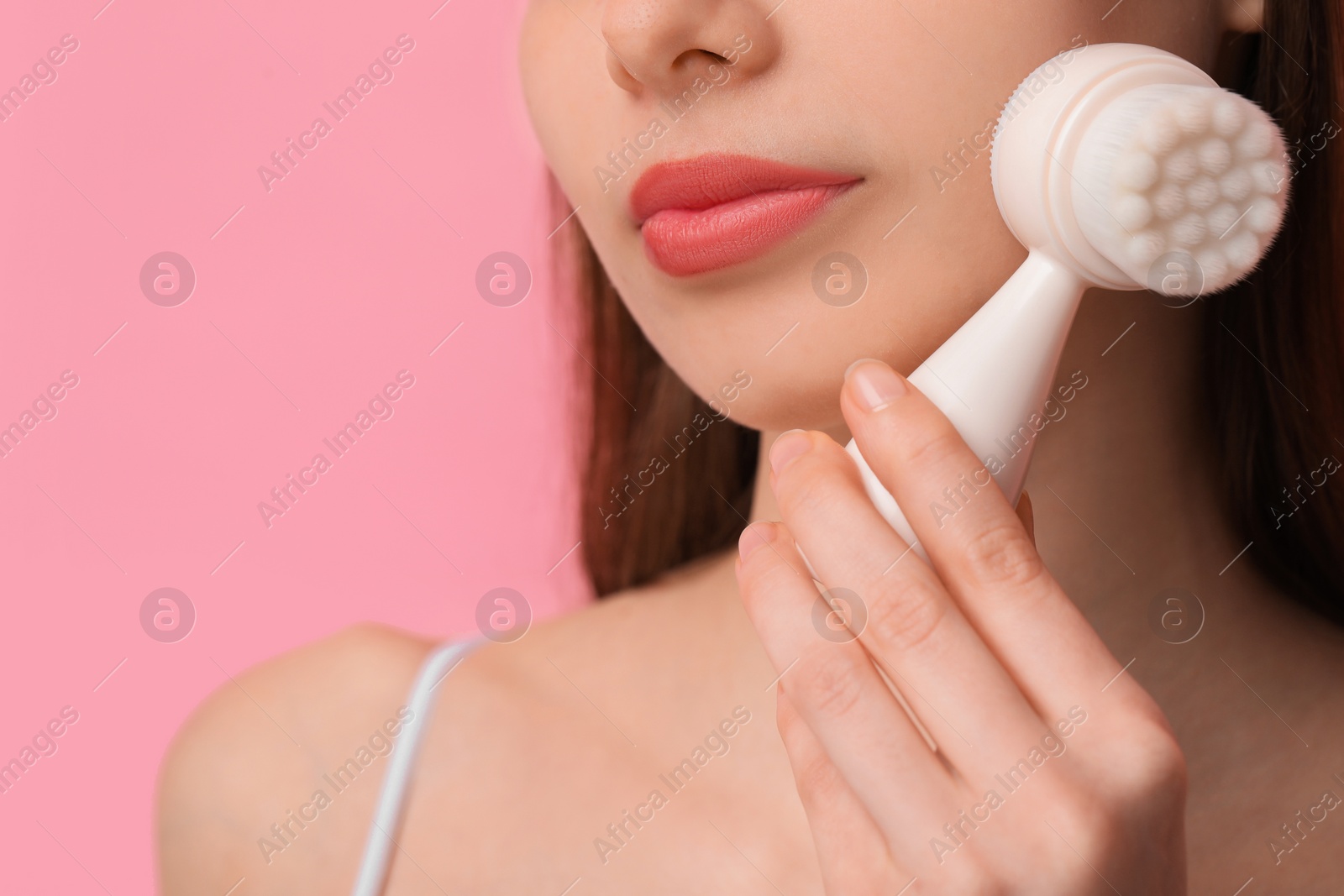 Photo of Washing face. Young woman with cleansing brush on pink background, closeup