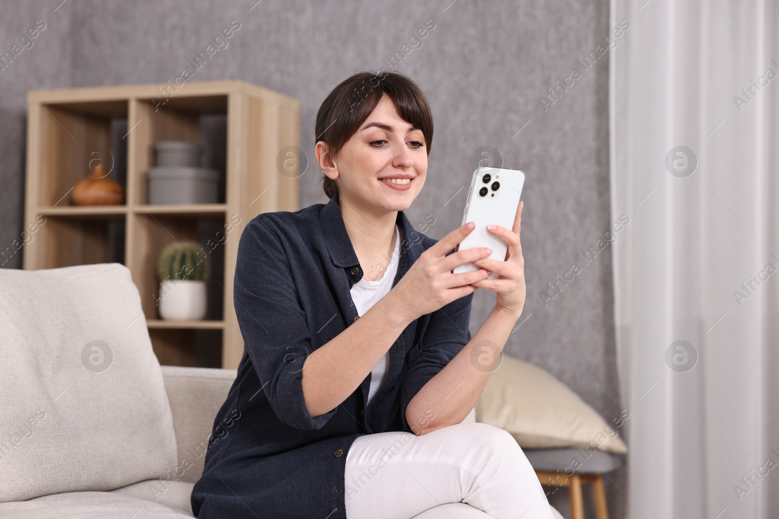 Photo of Beautiful young housewife using smartphone on sofa at home