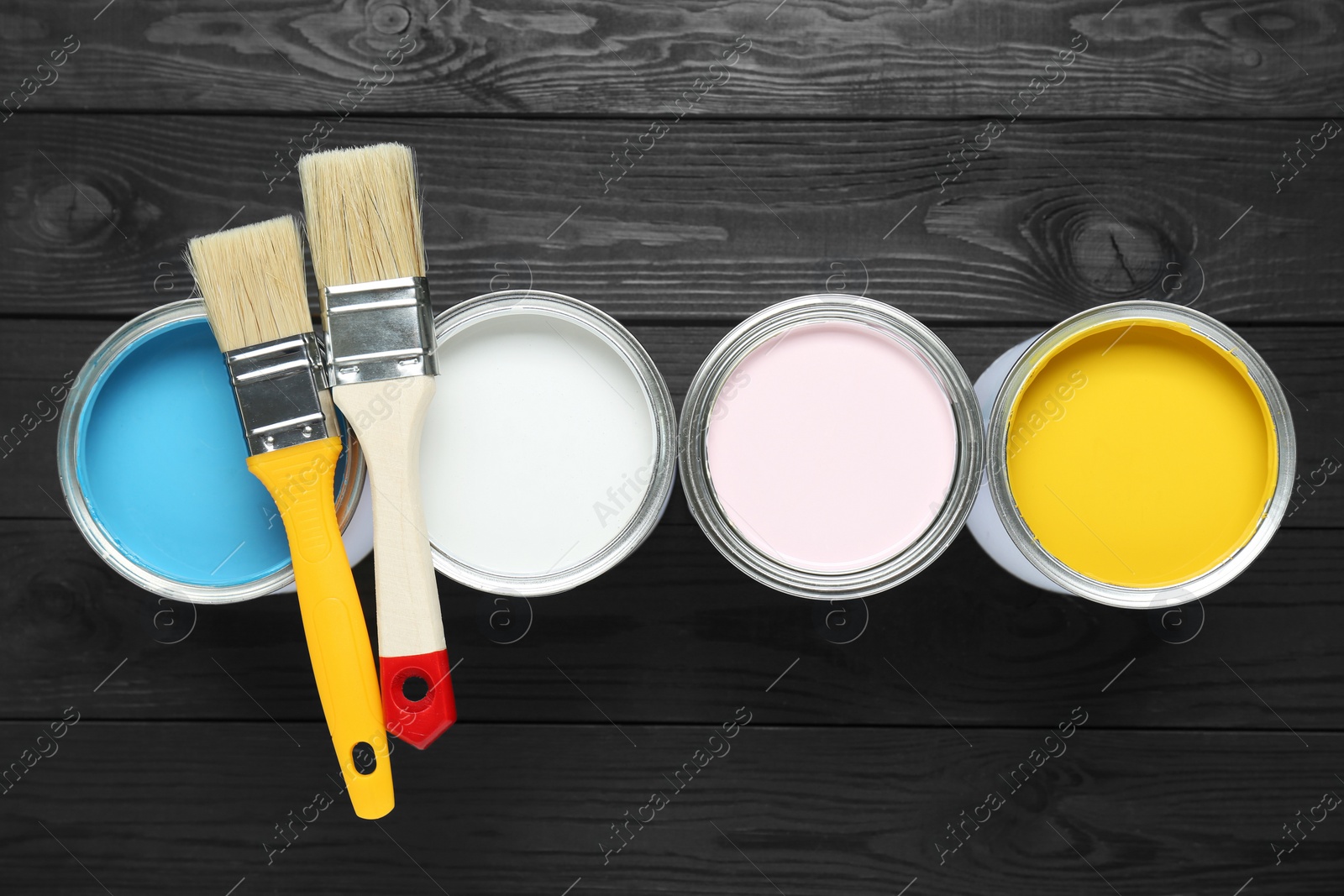Photo of Cans of colorful paints and brushes on black wooden table, flat lay