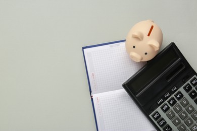 Photo of Calculator, notebook and piggy bank on light grey background, flat lay. Space for text
