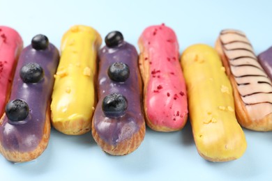 Delicious eclairs covered with glaze on light blue background, closeup