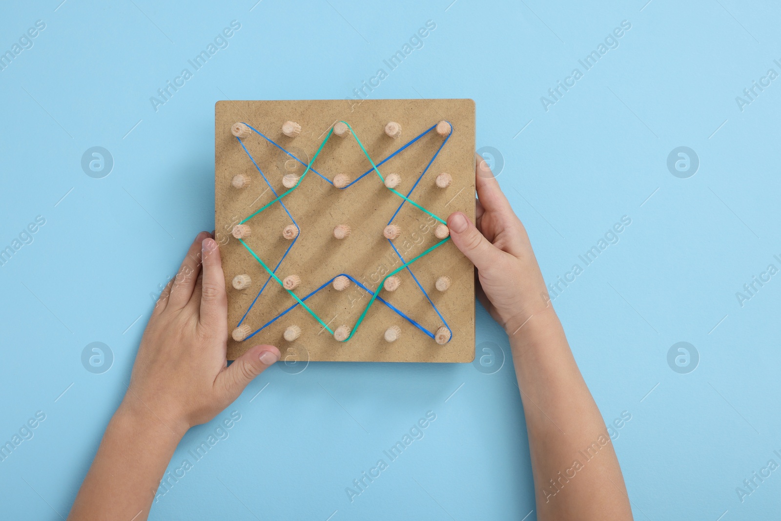 Photo of Motor skills development. Boy with geoboard and rubber bands at light blue table, top view