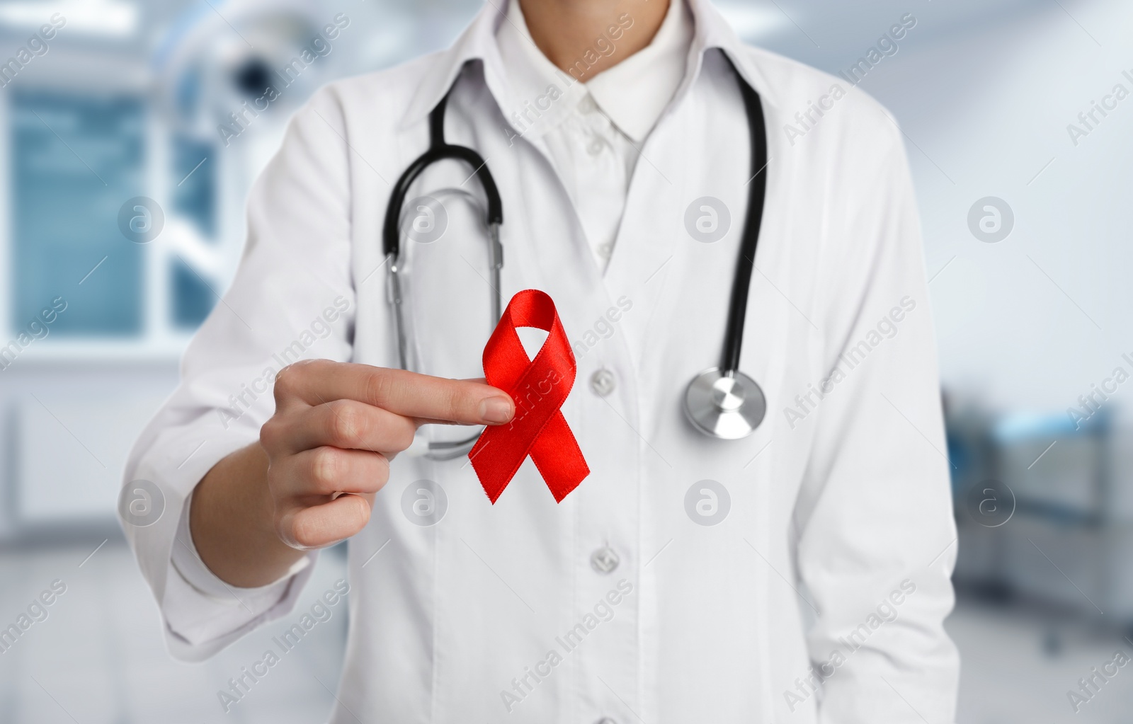 Image of Cancer awareness. Doctor holding red ribbon on blurred background, closeup