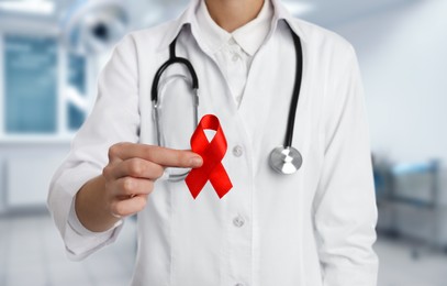 Image of Cancer awareness. Doctor holding red ribbon on blurred background, closeup