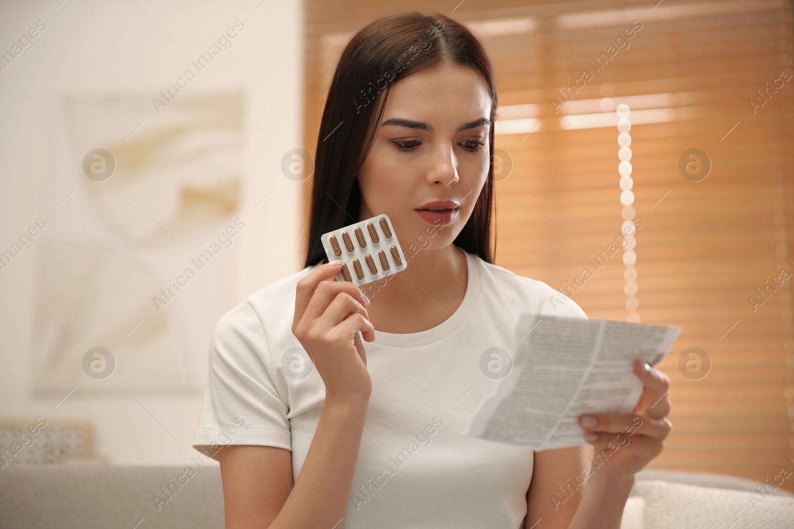 Photo of Young woman with pills reading medicine instruction at home