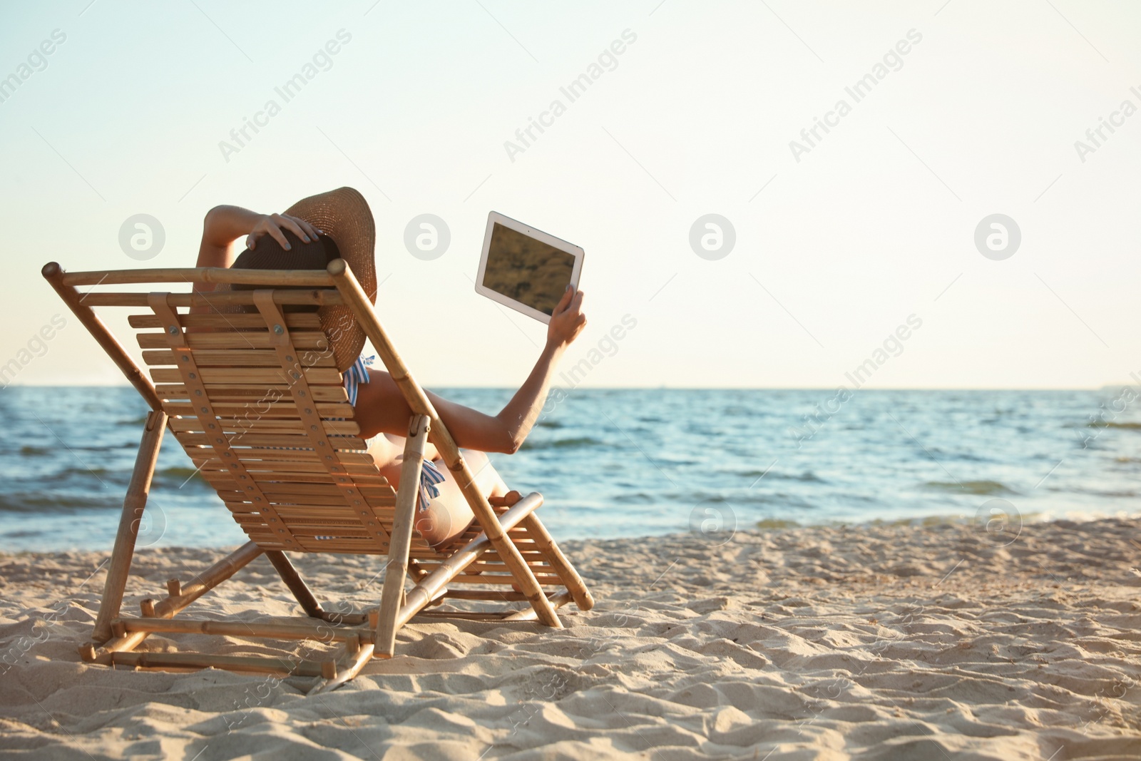 Photo of Young woman with tablet relaxing in deck chair on beach