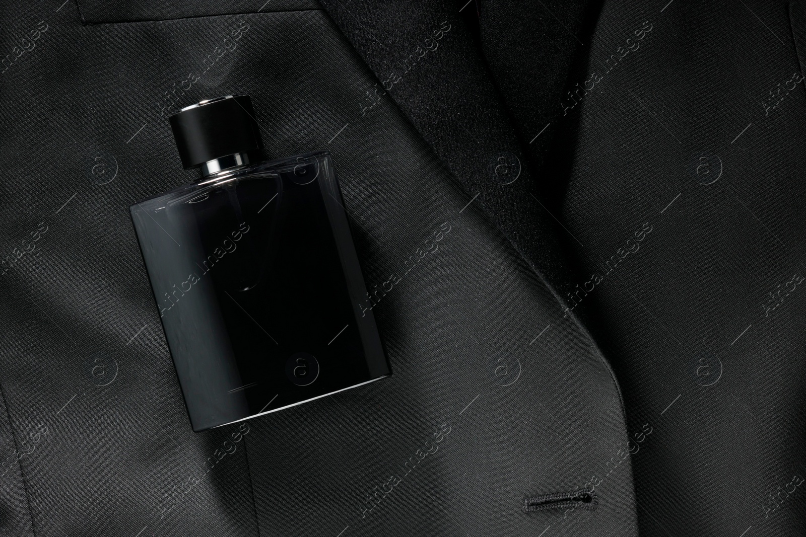 Photo of Luxury men's perfume in bottle on black jacket, top view. Space for text