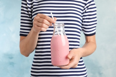 Woman with glass bottle of tasty smoothie on light blue background, closeup