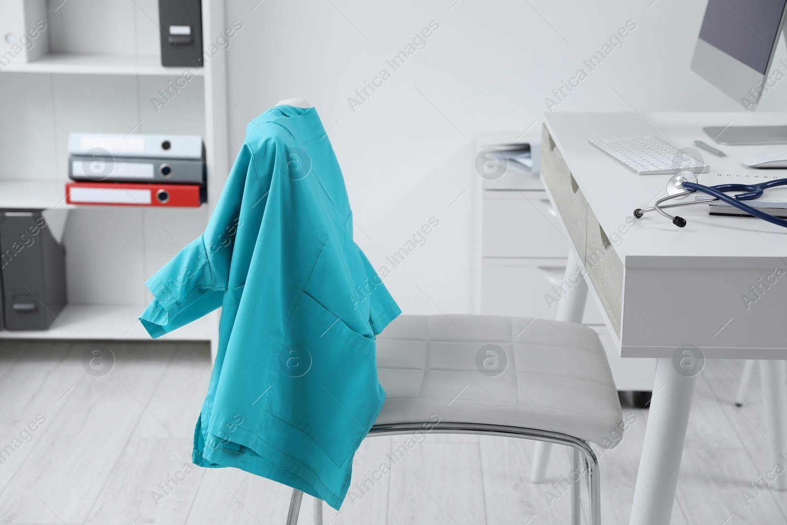 Photo of Turquoise medical uniform hanging on chair in clinic