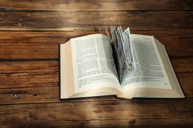 Photo of Open Bible with money on wooden table. Space for text