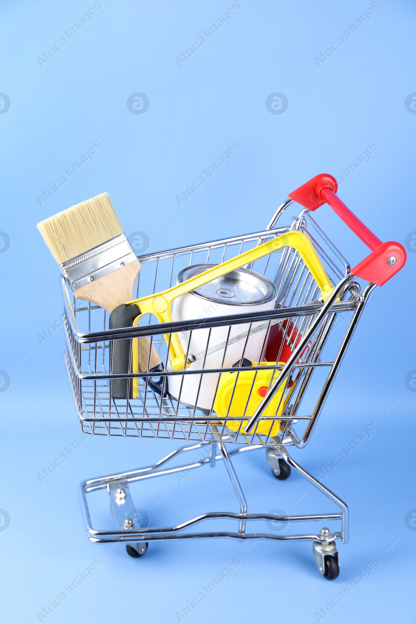 Photo of Small shopping cart with paint and renovation equipment on light blue background