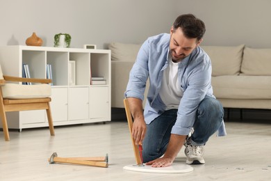 Photo of Man with screwdriver assembling table on floor at home. Space for text