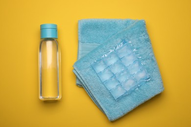 Photo of Bottle of water, ice pack and towel on yellow background, flat lay. Heat stroke treatment