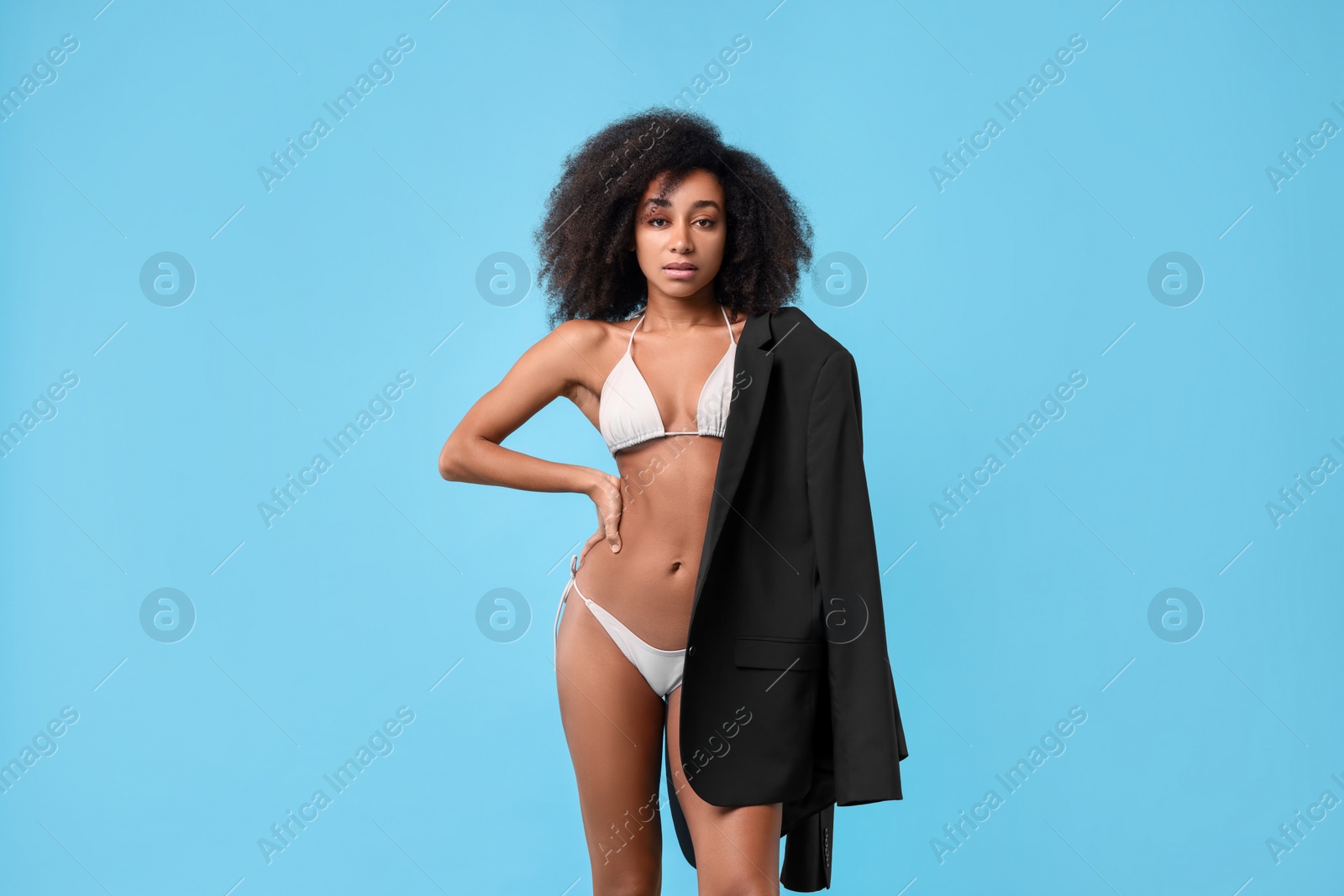 Photo of Beautiful woman in stylish bikini and jacket on light blue background