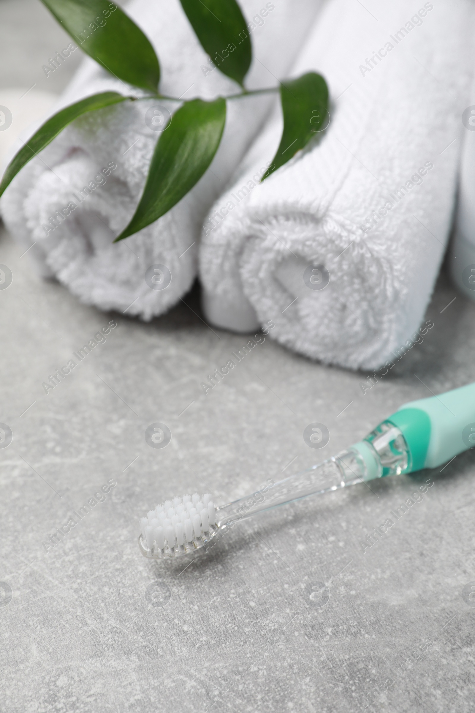 Photo of Electric toothbrush, rolled towels and green leaves on grey textured table, closeup