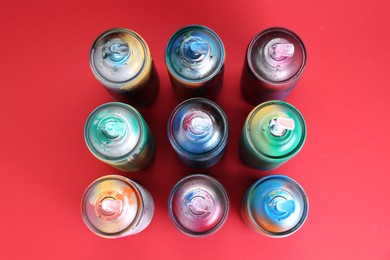Many spray paint cans on red background, flat lay